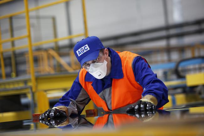 a man wearing a helmet, mask and protective gloves works in an AGC factory