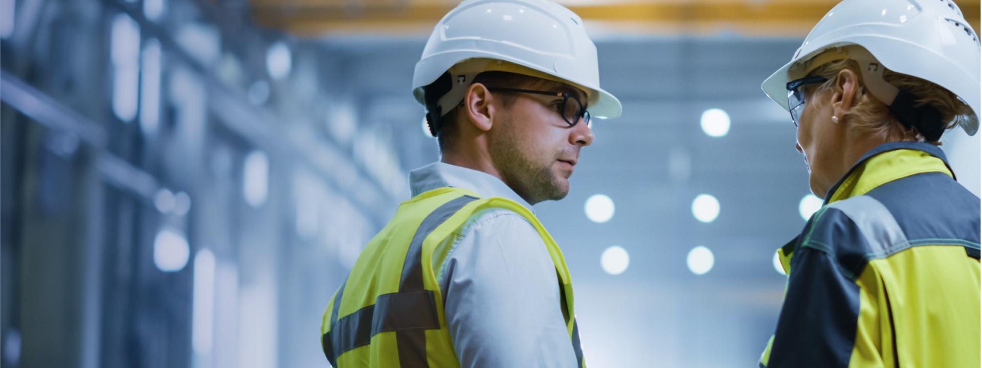 a man talking to a woman, both wearing yellow waistcoats and hard hats