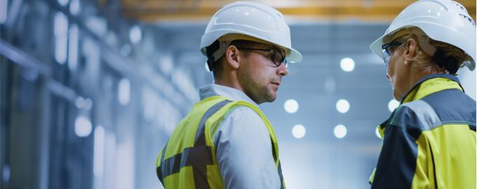 a man talking to a woman, both wearing yellow waistcoats and hard hats