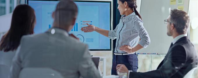 A woman shows a graph on a screen to 3 other people in a meeting room