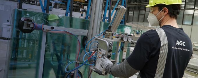 A man works in a AGC factory wearing a hard hat, a mask and protective goggles