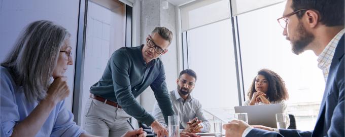 In a meeting room, 5 people discuss and take notes