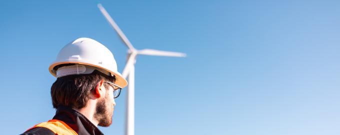 a worker wearing a hard hat and an orange waistcoat stands in front of the wind turbines