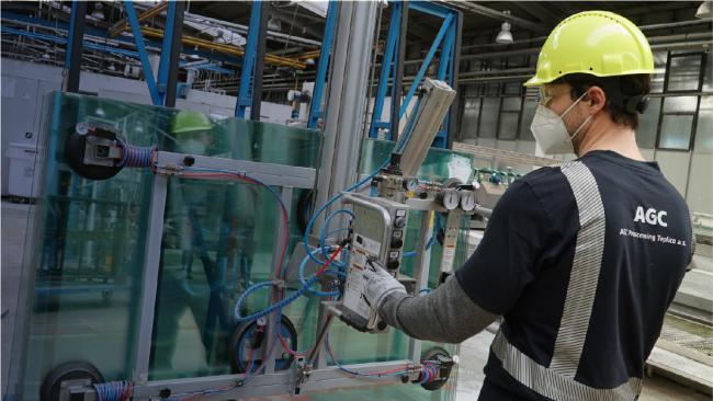 A man works in a AGC factory wearing a hard hat, a mask and protective goggles