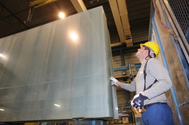 a man wearing a protective helmet and gloves works in an AGC factory