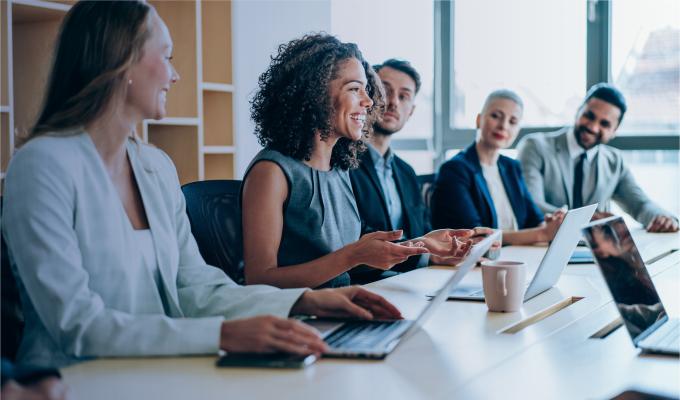 several people are in the meeting room listening to a smiling woman speak