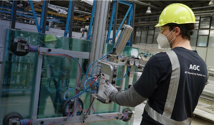 A man works in a AGC factory wearing a hard hat, a mask and protective goggles