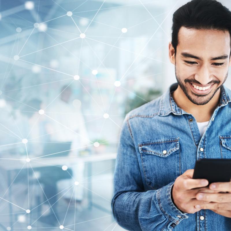 In his office, a man smiling with his mobile phone in his hand